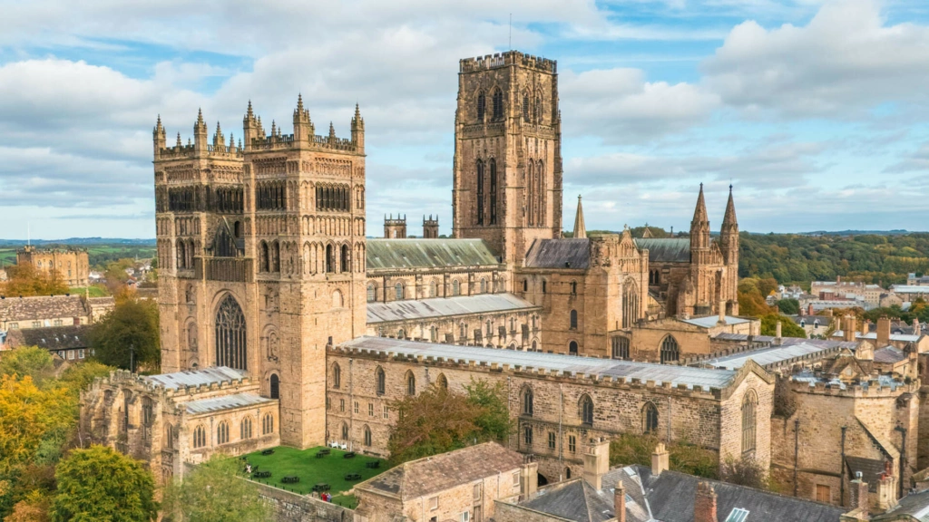 Durham cathedral and surrounding city buildings among green trees under a cloudy sky